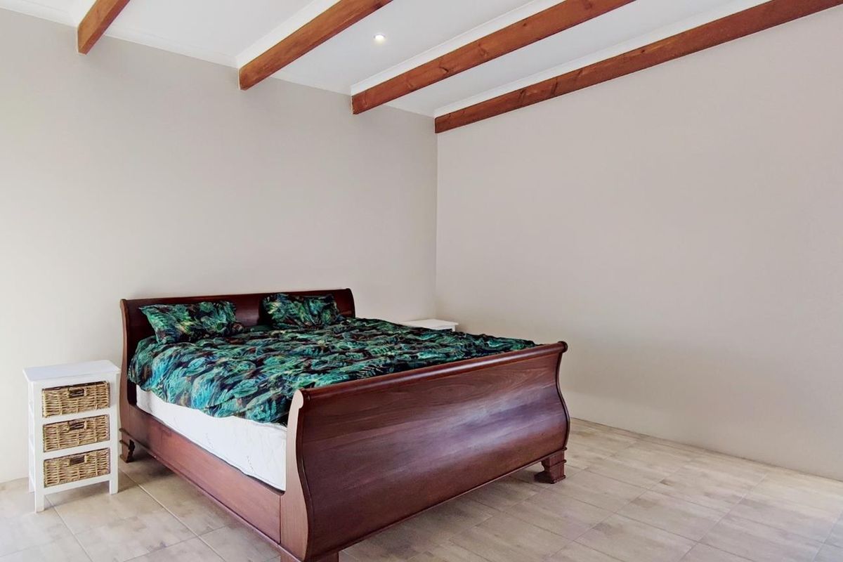 Spacious bedroom featuring exposed timber ceiling beams, neutral wall finishes, tiled flooring, and large windows providing natural light and scenic views.