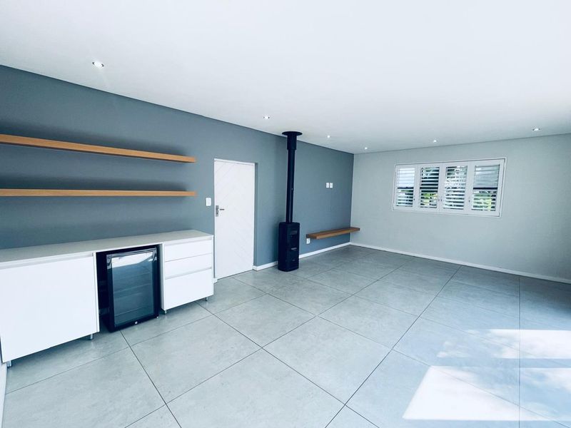 Spacious living area featuring large format floor tiles, a modern freestanding fireplace, built-in cabinetry with floating shelves, and plantation-style shutter blinds.