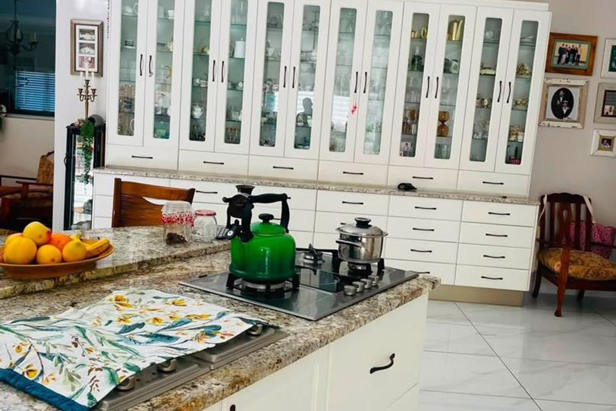 Spacious kitchen featuring a large island with granite countertops, extensive white cabinetry with glass-front displays, and modern porcelain floor tiles.