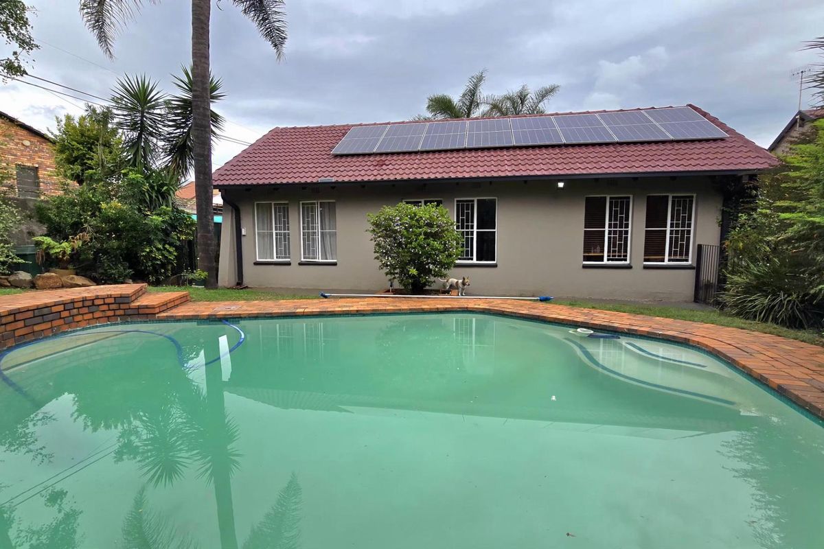 Rear view of the property featuring a swimming pool with brick coping and a tiled roof house equipped with solar panels.