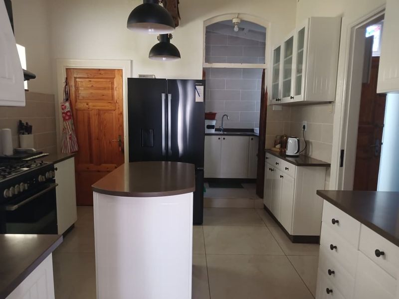 A functional kitchen featuring a central island, white cabinetry, tiled flooring, and a convenient adjoining scullery area with additional sink and storage.
