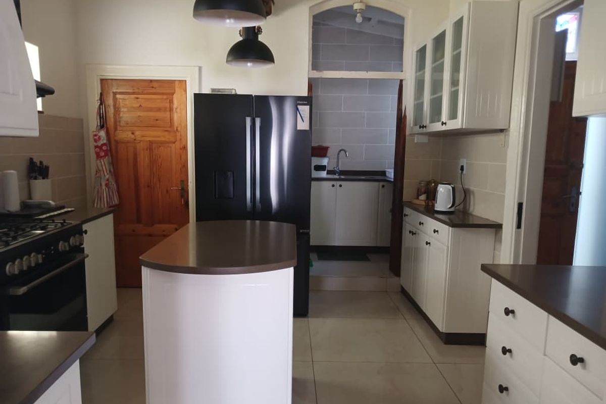 A functional kitchen featuring a central island, white cabinetry, tiled flooring, and a convenient adjoining scullery area with additional sink and storage.