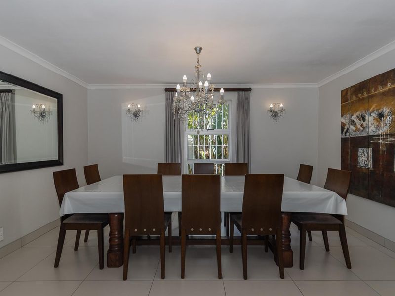 A formal dining room featuring neutral tiled flooring, cove cornicing, and elegant lighting fixtures including a central crystal chandelier and matching wall sconces.