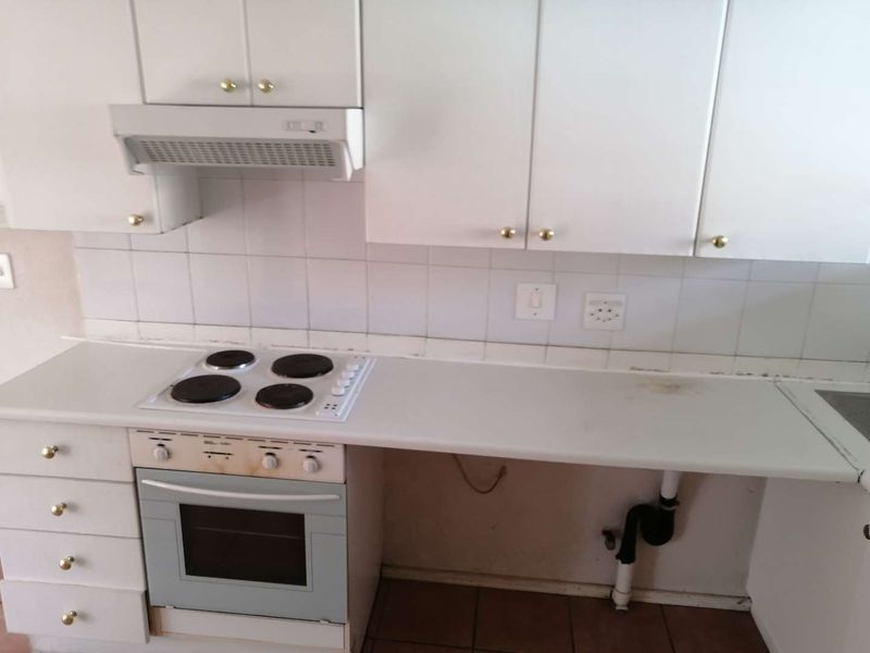A dated kitchen featuring white cabinetry, an integrated electric hob and oven, and a tiled backsplash, requiring cosmetic updates to modernize the space.