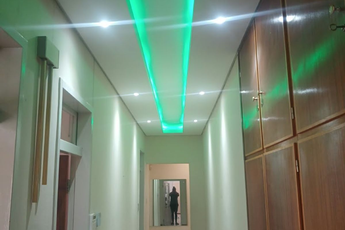 A well-lit hallway featuring built-in wooden storage cabinetry, tiled flooring, and modern recessed ceiling lighting with decorative green accent lighting.