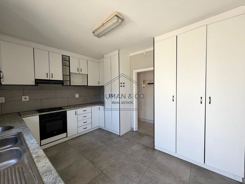 A clean, functional kitchen featuring white cabinetry, granite countertops, built-in oven with gas hob, and ample storage space with a large pantry cupboard.