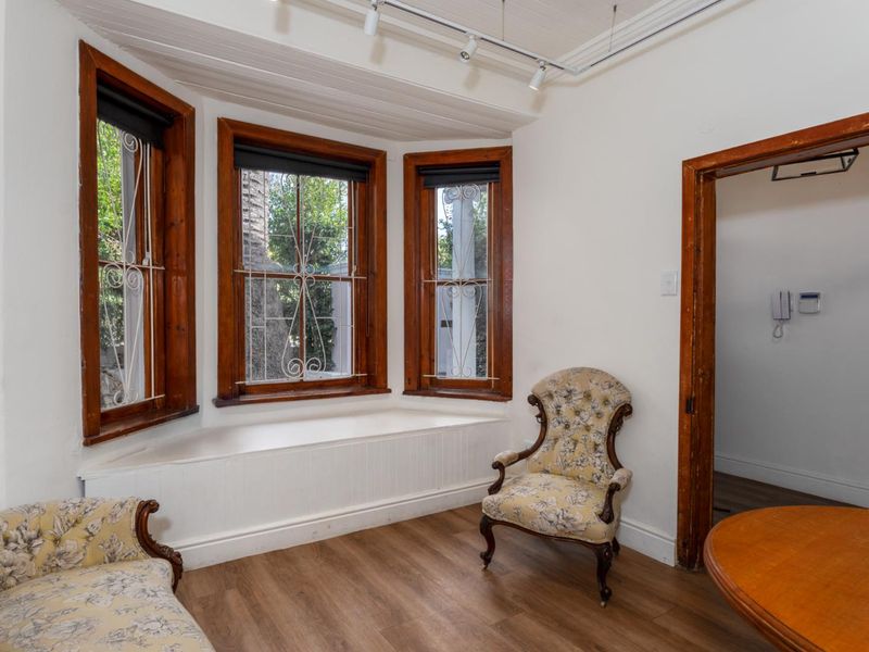 A bright living area featuring a classic bay window with a built-in seat, timber flooring, and track lighting.
