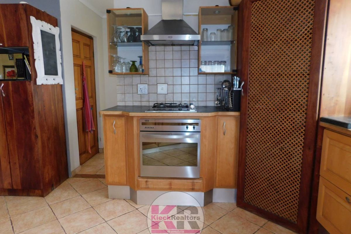 A functional kitchen area featuring wooden cabinetry, a built-in oven, gas hob, stainless steel extractor fan, and tiled flooring.