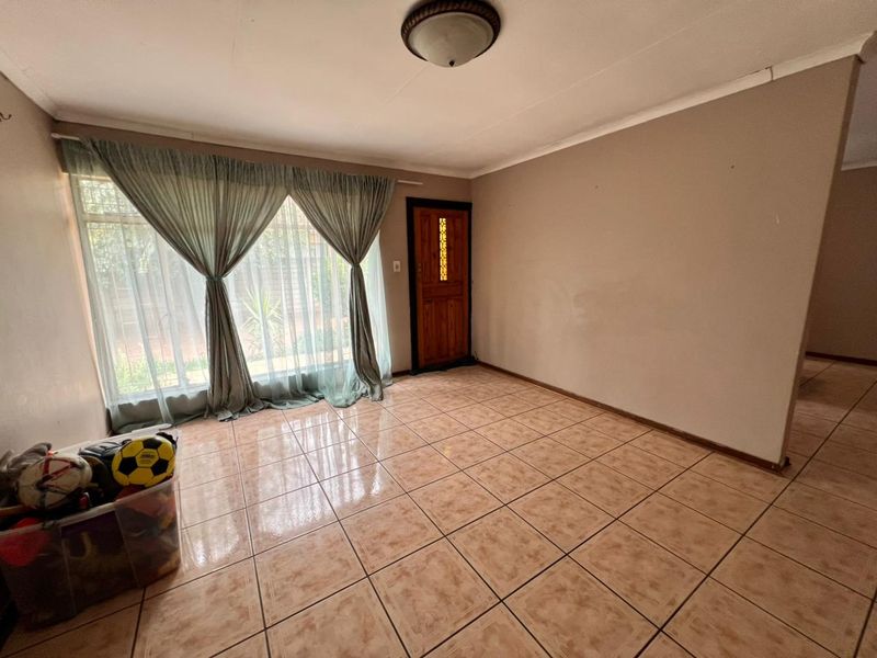 A spacious, empty living room featuring ceramic floor tiles, a flush mount ceiling light, and a wooden front door with a glass insert.