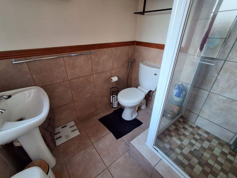 A functional bathroom featuring a pedestal basin, toilet, and a glass-enclosed shower with neutral ceramic tiling throughout.