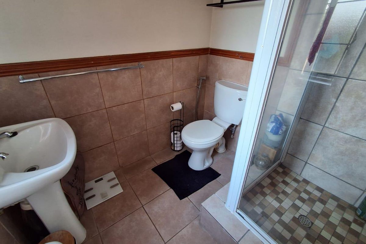 A functional bathroom featuring a pedestal basin, toilet, and a glass-enclosed shower with neutral ceramic tiling throughout.