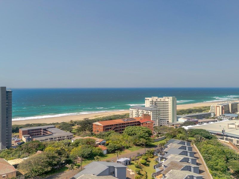 Elevated coastal view overlooking the ocean, sandy beach, and surrounding residential apartment buildings.