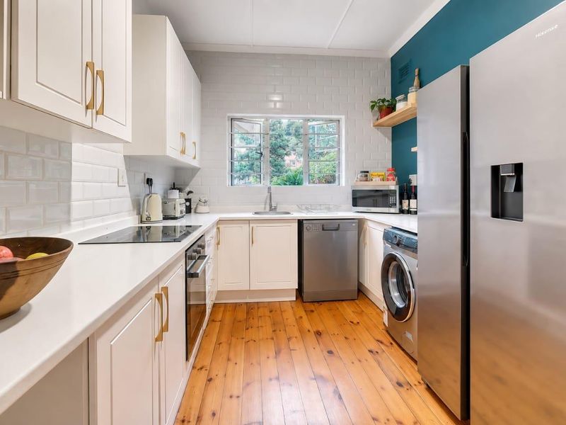 A well-maintained kitchen featuring white shaker-style cabinetry, subway tile backsplash, timber flooring, and modern integrated appliances.