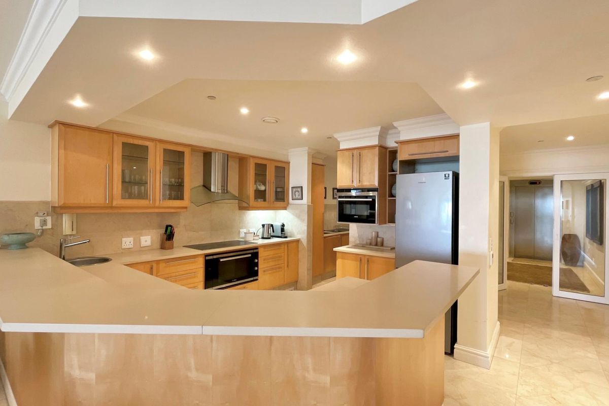 Spacious kitchen featuring light wood cabinetry, stone countertops, integrated oven, hob, and extractor fan, with a breakfast bar and tiled flooring.