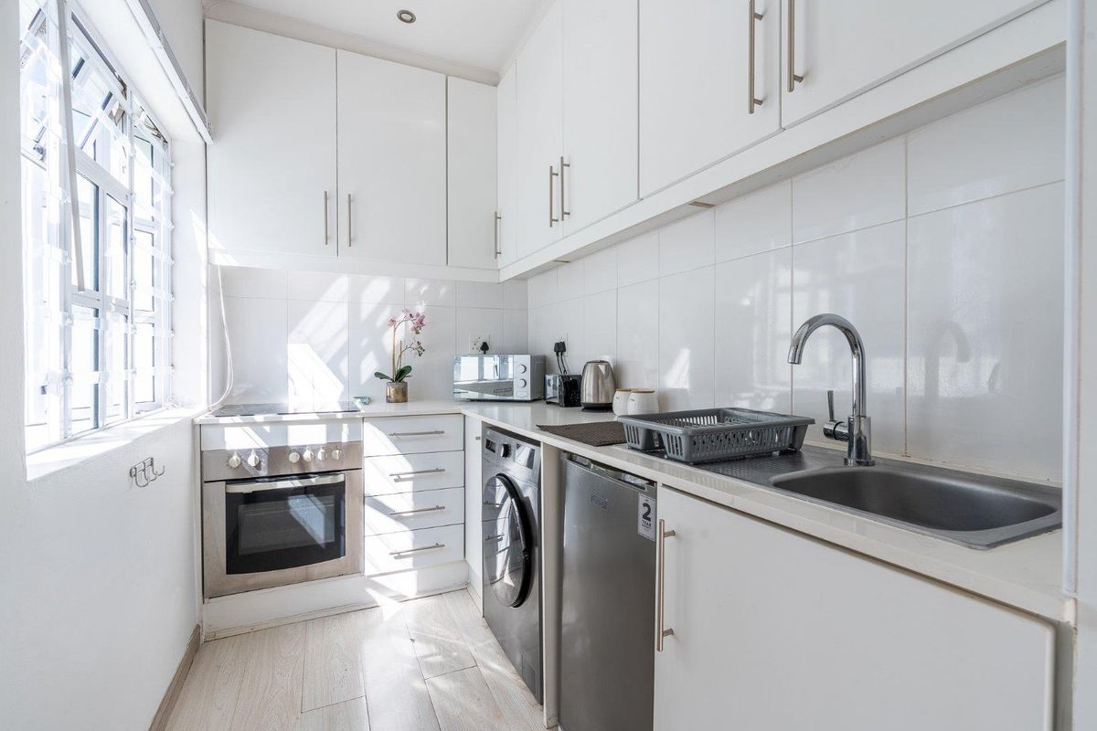 A compact, well-maintained kitchen featuring white cabinetry, a stainless steel sink, built-in oven, and electric hob with tiled splashbacks and laminate flooring.