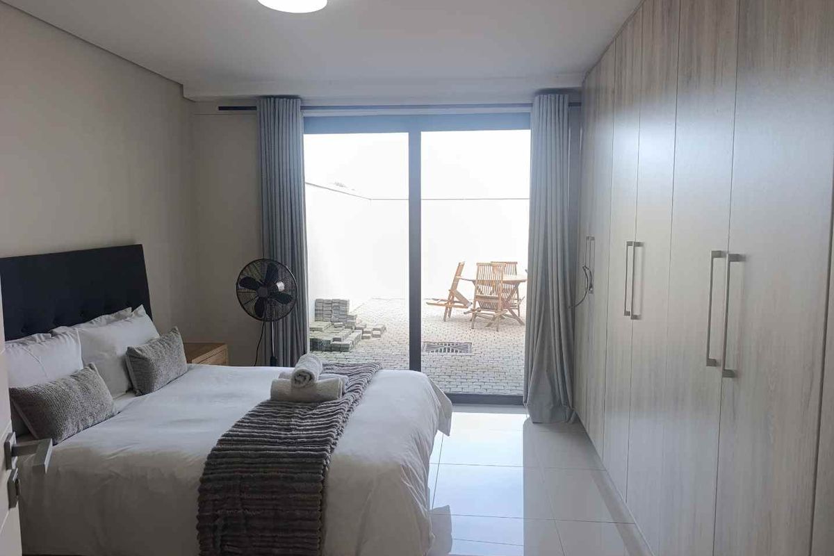 Modern bedroom featuring extensive built-in cupboards, sleek tiled flooring, and a large sliding glass door providing direct access to an outdoor patio area.