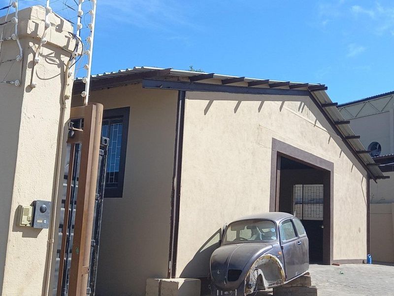 Front exterior view of an industrial property featuring a secure gated entrance, perimeter wall with electric fencing, and paved yard area.