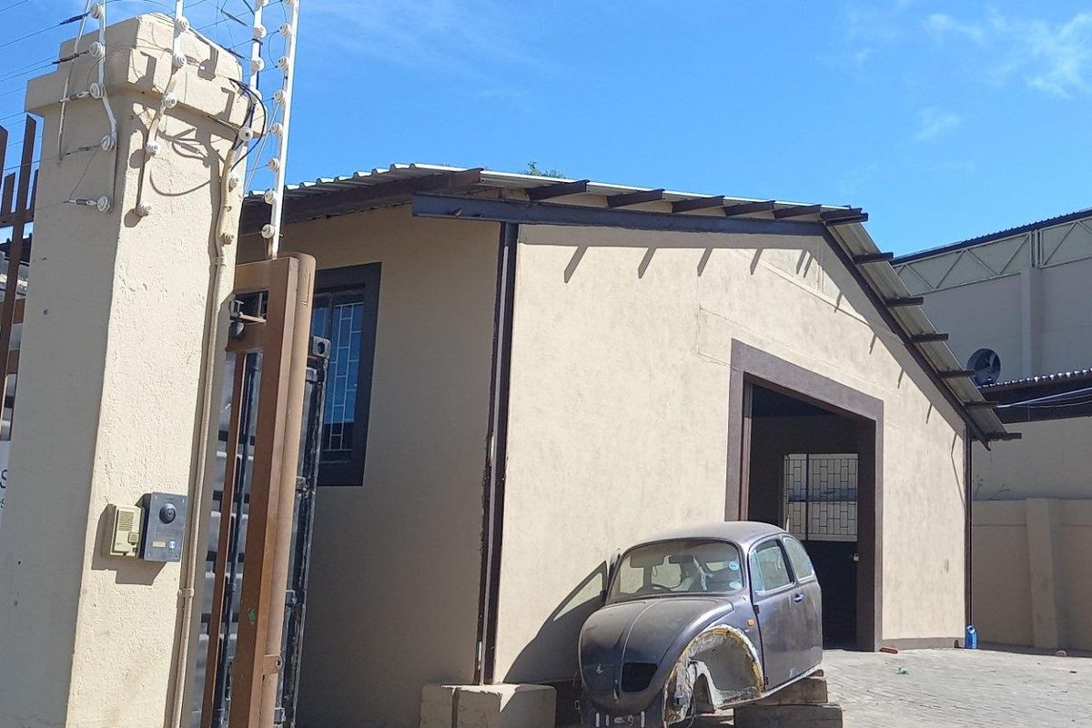 Front exterior view of an industrial property featuring a secure gated entrance, perimeter wall with electric fencing, and paved yard area.