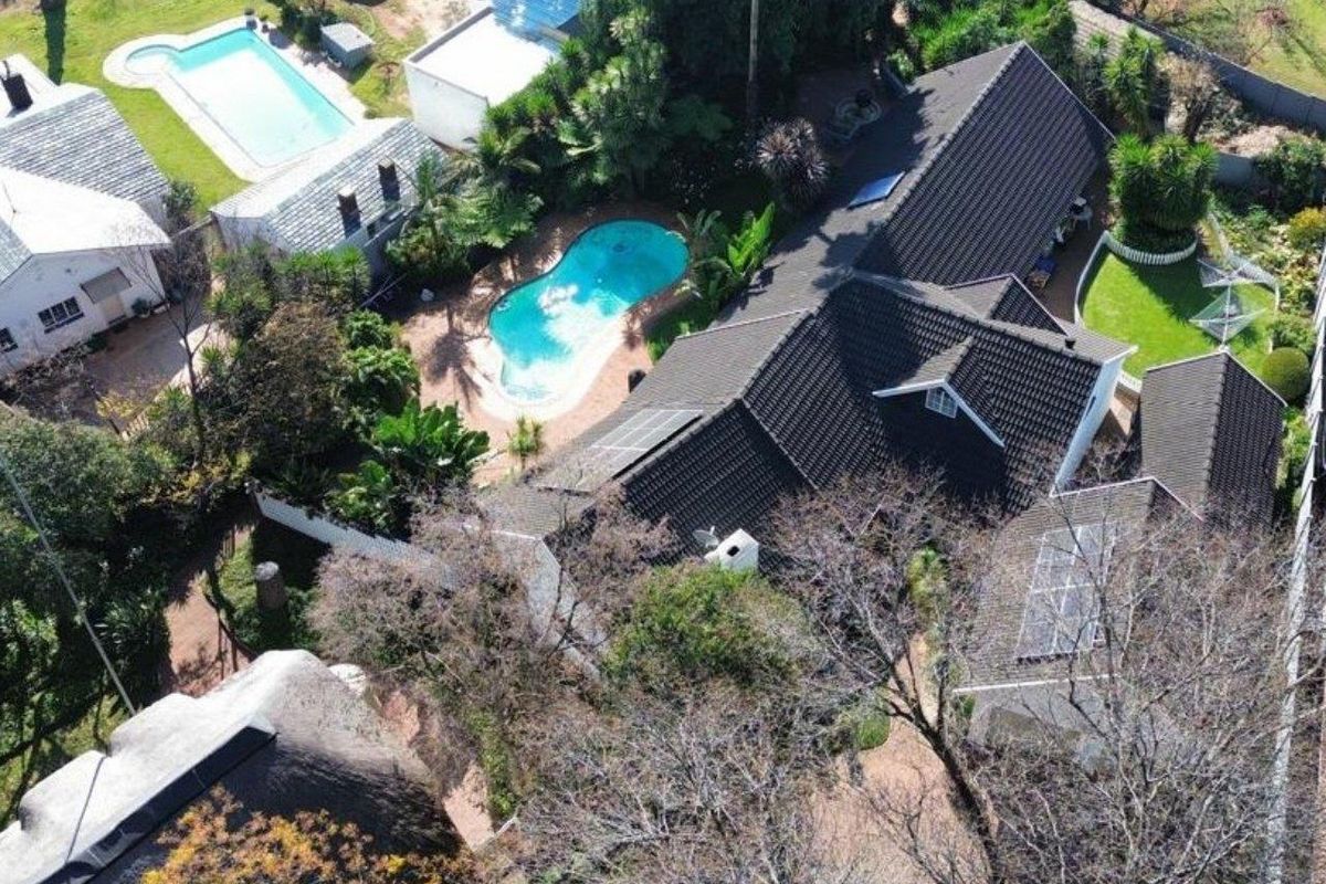 Aerial view of the property showcasing the main residence, swimming pool, landscaped garden areas, and tiled roof structure.