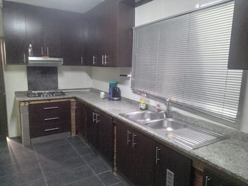 A functional kitchen featuring dark wood cabinetry, granite countertops, a stainless steel double sink, and a gas hob with an extractor fan.