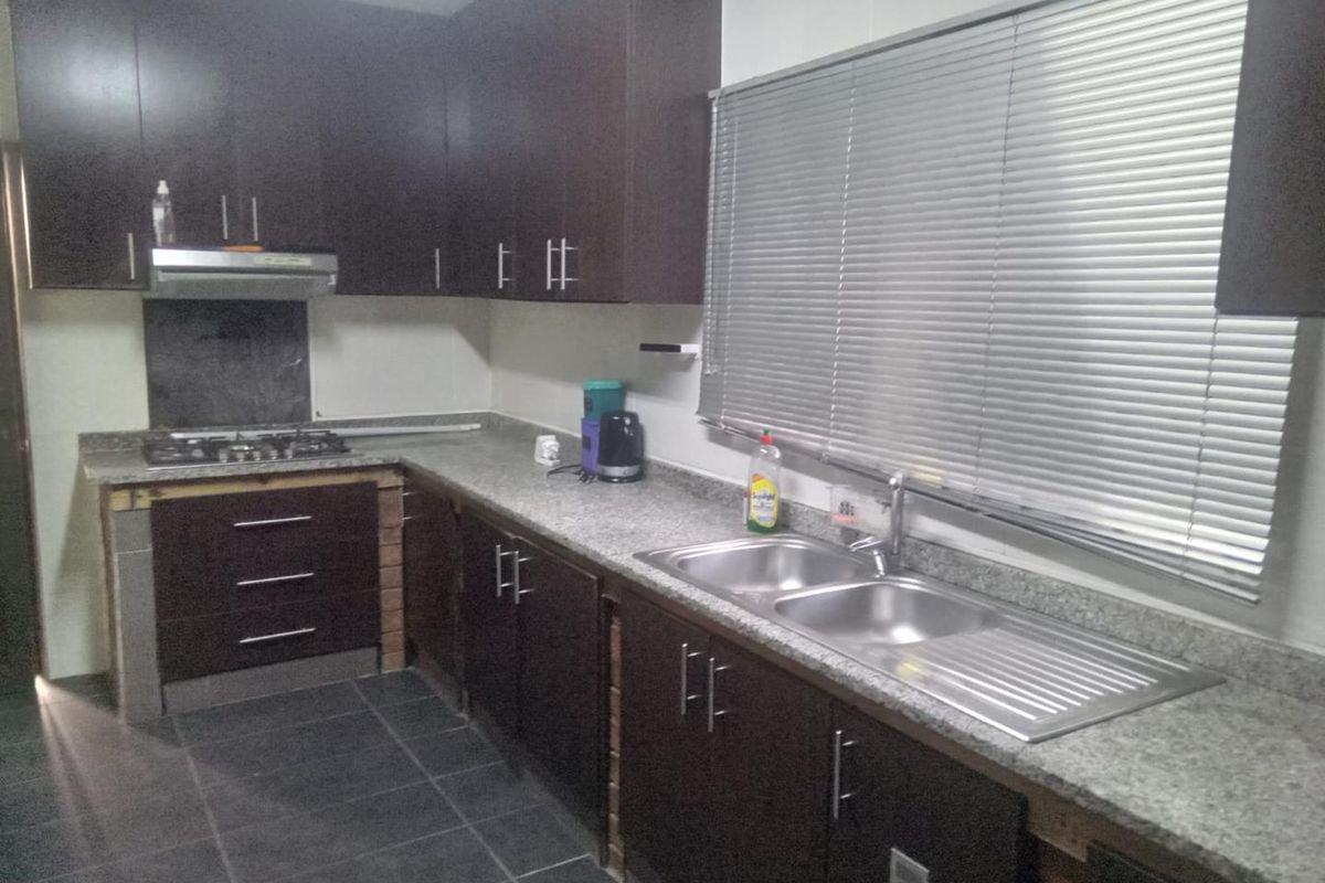 A functional kitchen featuring dark wood cabinetry, granite countertops, a stainless steel double sink, and a gas hob with an extractor fan.