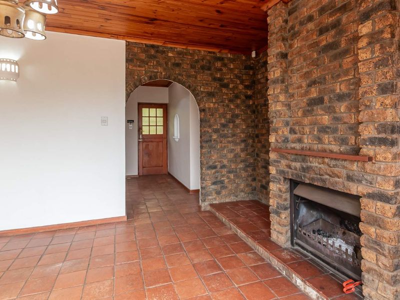 Spacious living area featuring a prominent exposed brick fireplace, terracotta floor tiles, and a warm timber ceiling with an arched entrance.