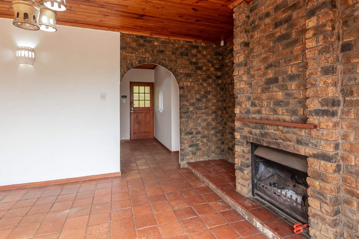 Spacious living area featuring a prominent exposed brick fireplace, terracotta floor tiles, and a warm timber ceiling with an arched entrance.