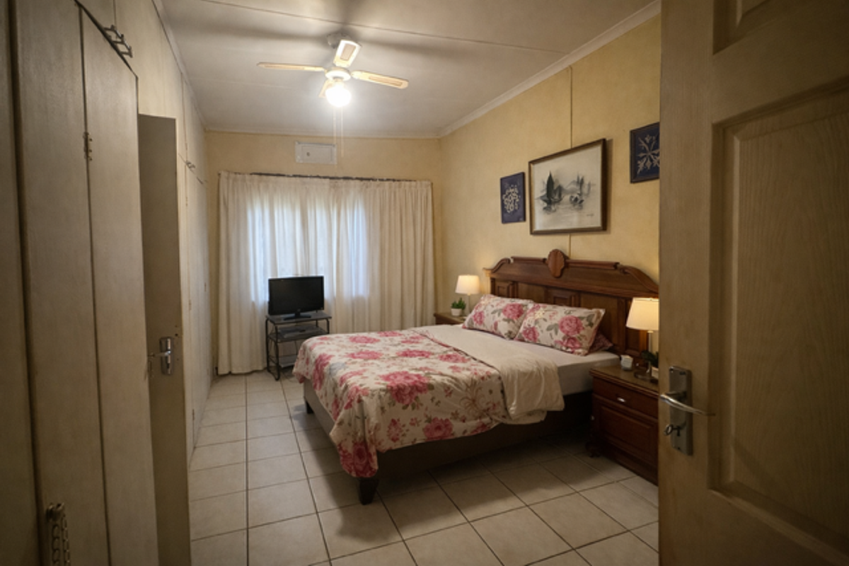 A functional bedroom featuring built-in cupboards, tiled flooring, and a ceiling fan, offering a comfortable and practical living space.