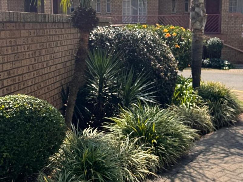 A well-maintained front exterior view featuring brick paving, a solid brick boundary wall, and established garden landscaping.