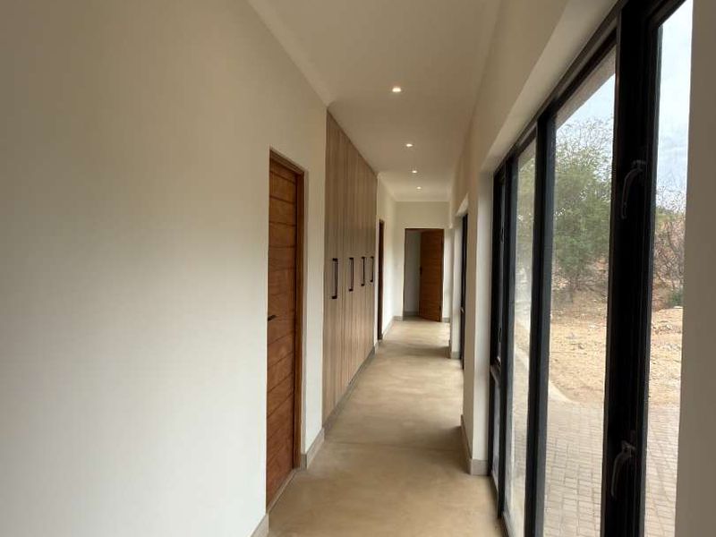 A modern, sunlit hallway featuring polished concrete floors, extensive built-in cabinetry, and large floor-to-ceiling windows overlooking the exterior.