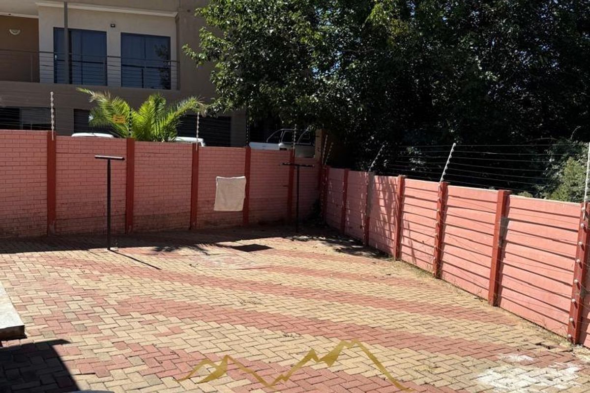 A paved rear courtyard area featuring perimeter brick boundary walls with integrated electric fencing.