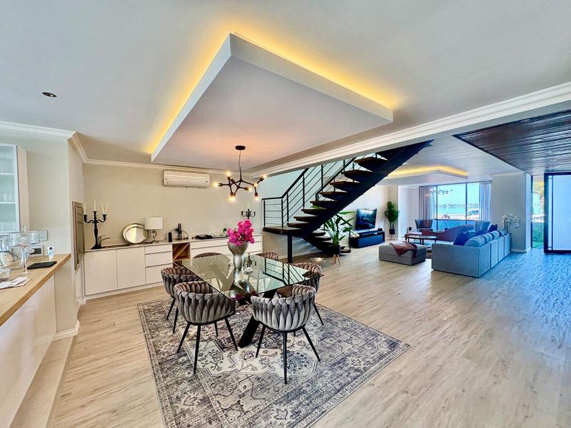 Spacious open-plan living and dining area featuring a modern floating staircase, recessed ceiling lighting, and sleek built-in cabinetry with high-quality finishes.