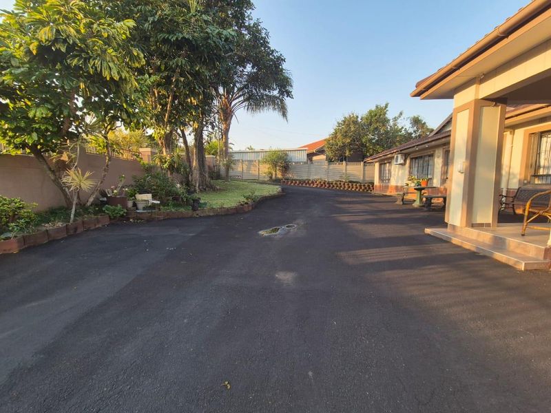 Spacious asphalt driveway leading to the front entrance of the house, featuring a covered porch and established garden perimeter.
