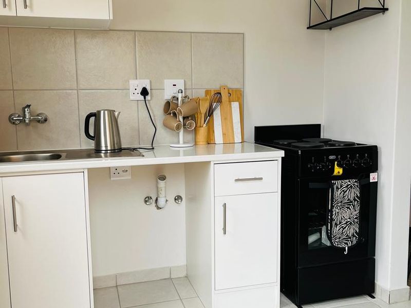 A compact kitchen featuring white cabinetry, tiled backsplash, a stainless steel sink, and a black freestanding stove with tiled flooring.
