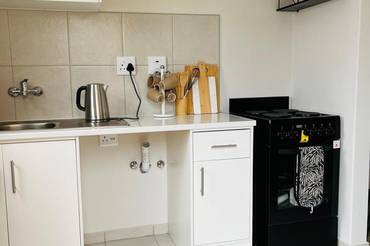 A compact kitchen featuring white cabinetry, tiled backsplash, a stainless steel sink, and a black freestanding stove with tiled flooring.
