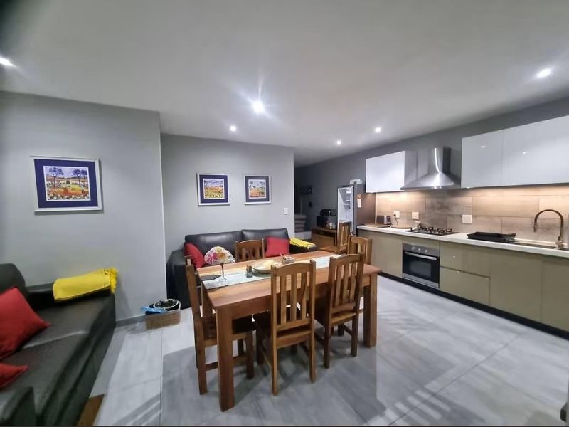 Modern open-plan living and dining area featuring a sleek kitchen with built-in cabinetry, gas hob, and high-quality tiled flooring throughout.