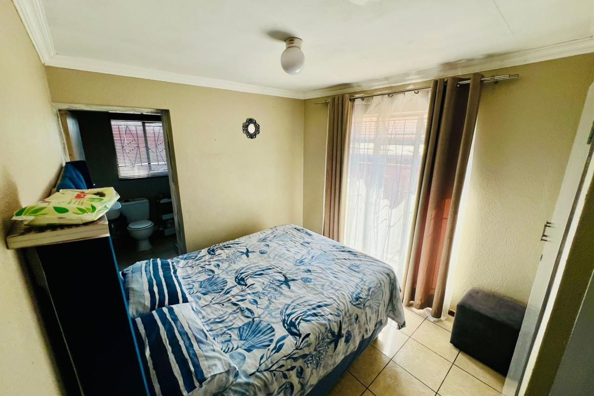 A bedroom featuring tiled flooring, a sliding door with curtains, and an en-suite bathroom access.