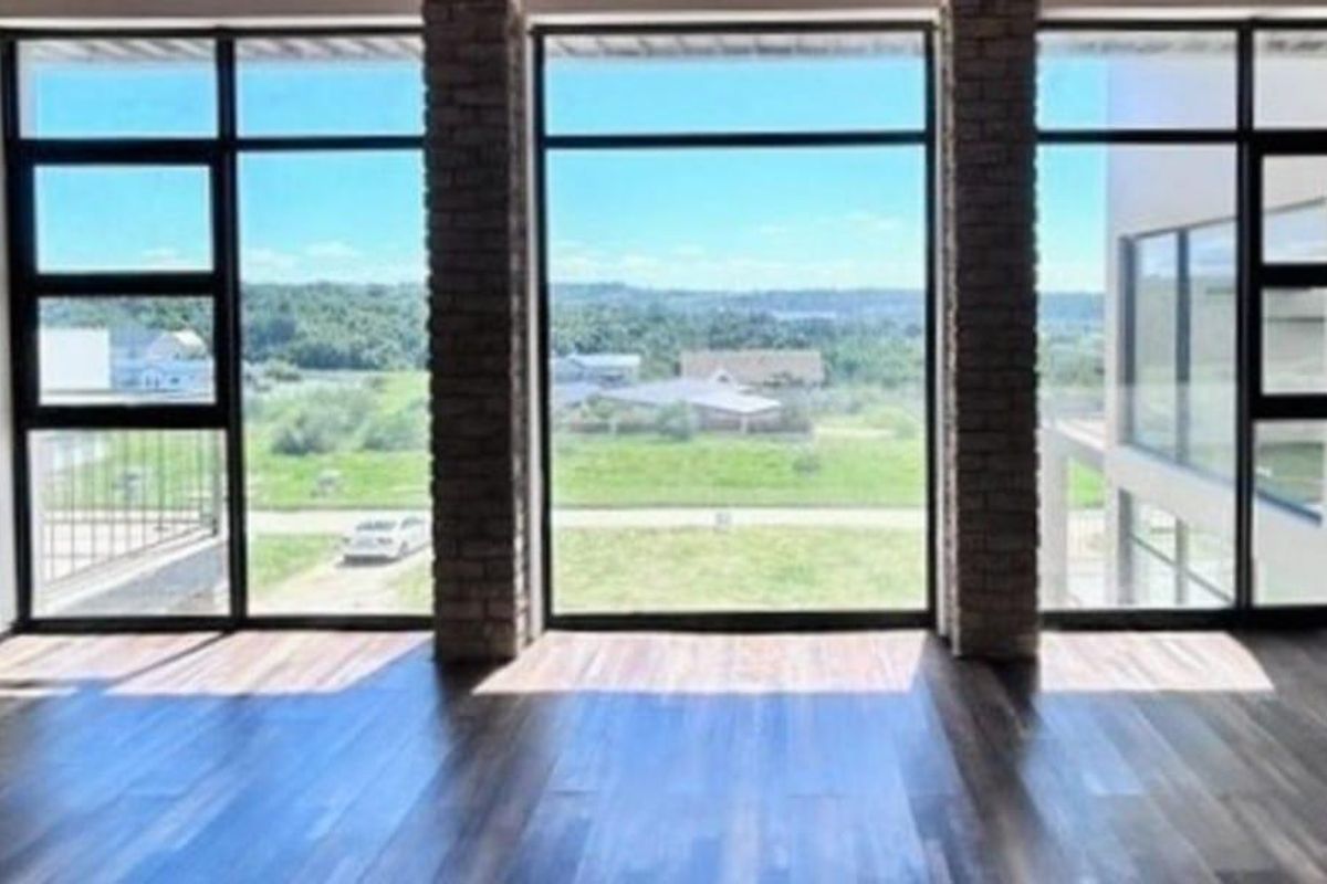 Spacious interior area featuring large floor-to-ceiling windows with brick pillar accents and modern wood-look flooring, offering expansive views of the surrounding landscape.