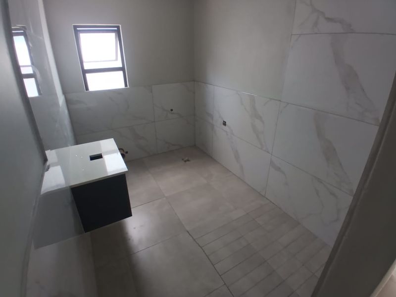 An unfinished bathroom featuring wall-mounted vanity cabinetry, marble-look wall tiling, and floor tiles, awaiting final plumbing fixtures and basin installation.