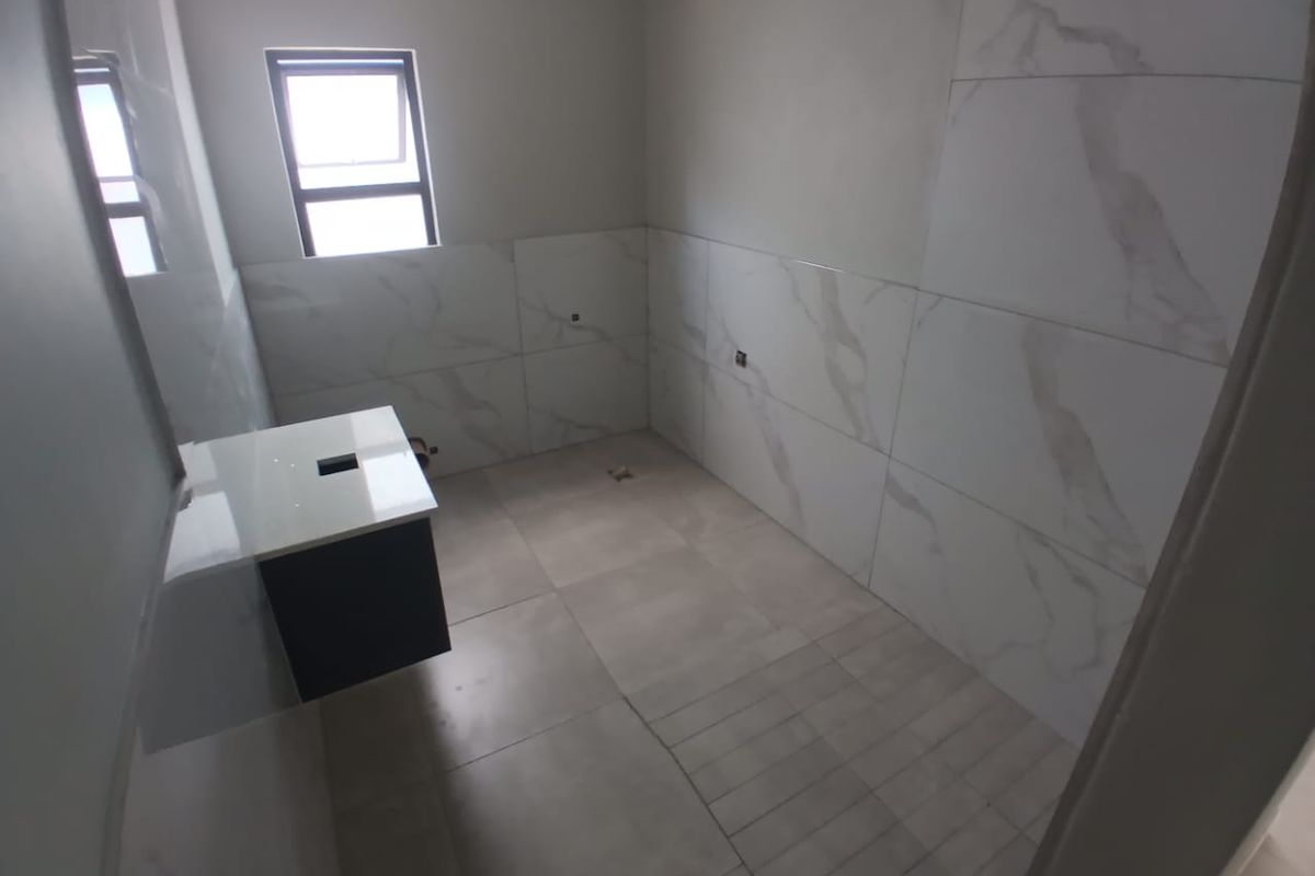 An unfinished bathroom featuring wall-mounted vanity cabinetry, marble-look wall tiling, and floor tiles, awaiting final plumbing fixtures and basin installation.