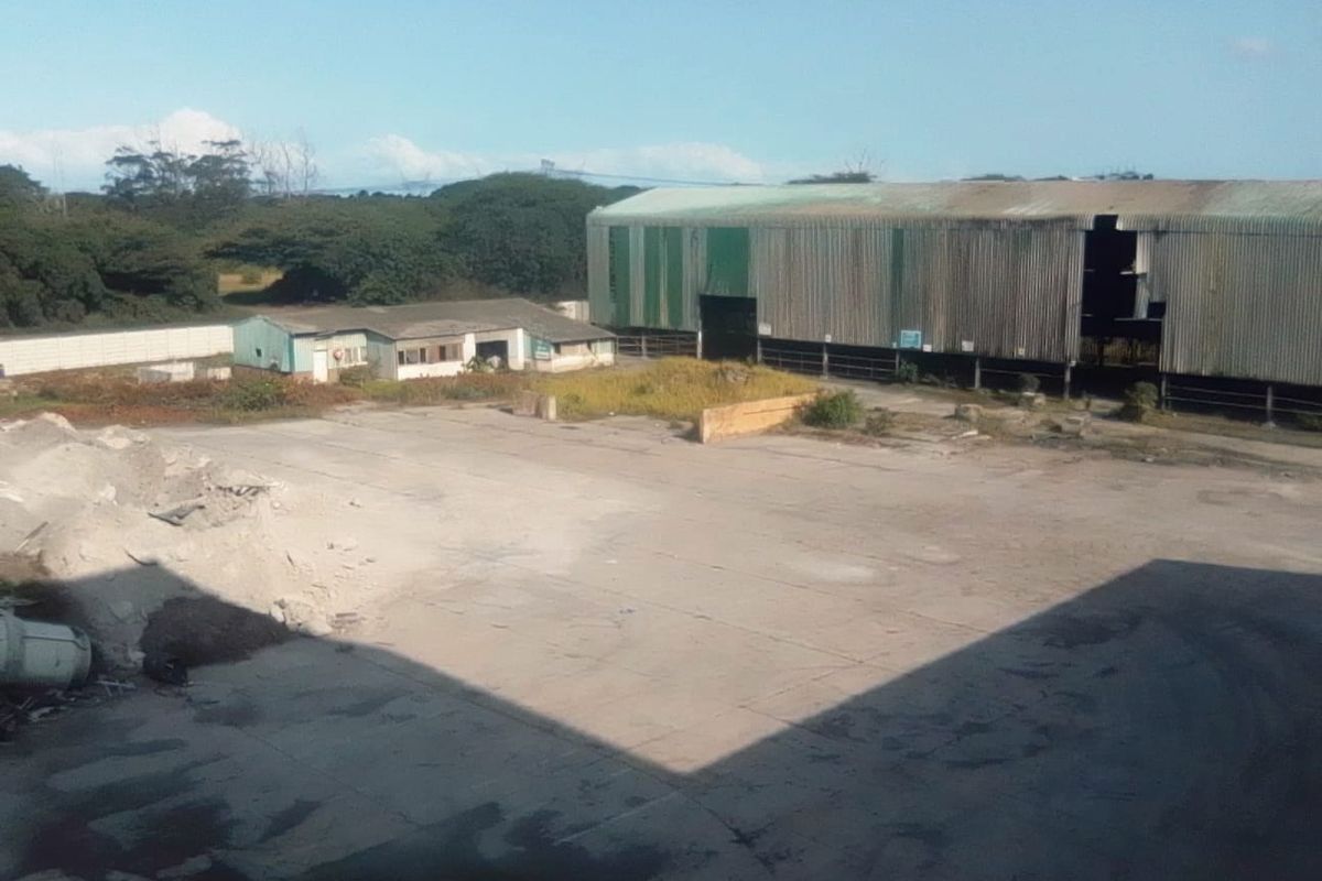 Industrial site featuring a large warehouse structure with metal cladding, an expansive concrete yard, and secondary outbuildings on a spacious plot.