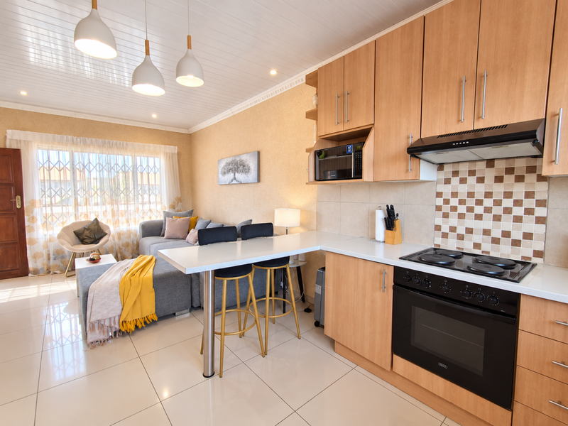 Modern open-plan living area featuring a well-equipped kitchen with built-in appliances, breakfast bar, and bright, tiled flooring throughout the space.