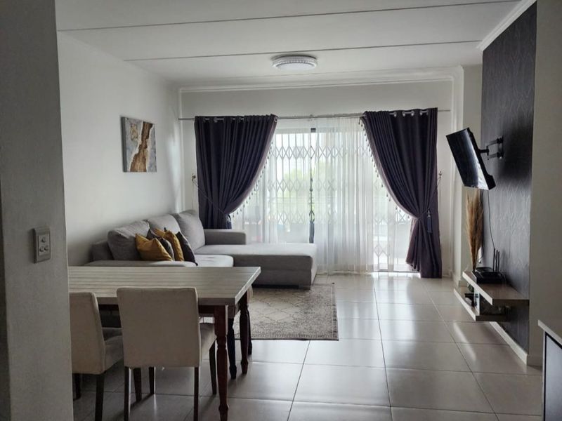 An open-plan living and dining area featuring tiled flooring, a feature wall, and direct access to a balcony through a sliding glass door.