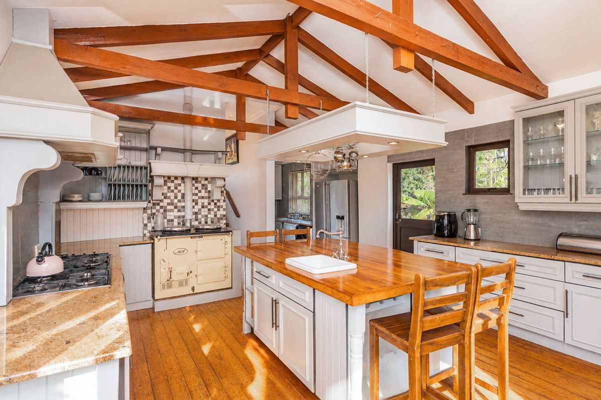 Spacious country-style kitchen featuring exposed timber ceiling beams, a central island with a farmhouse sink, and a classic range cooker.