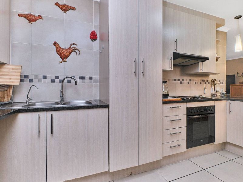 A functional kitchen featuring light wood-finish cabinetry, granite countertops, a built-in oven with gas hob, and a double sink with tiled backsplash.