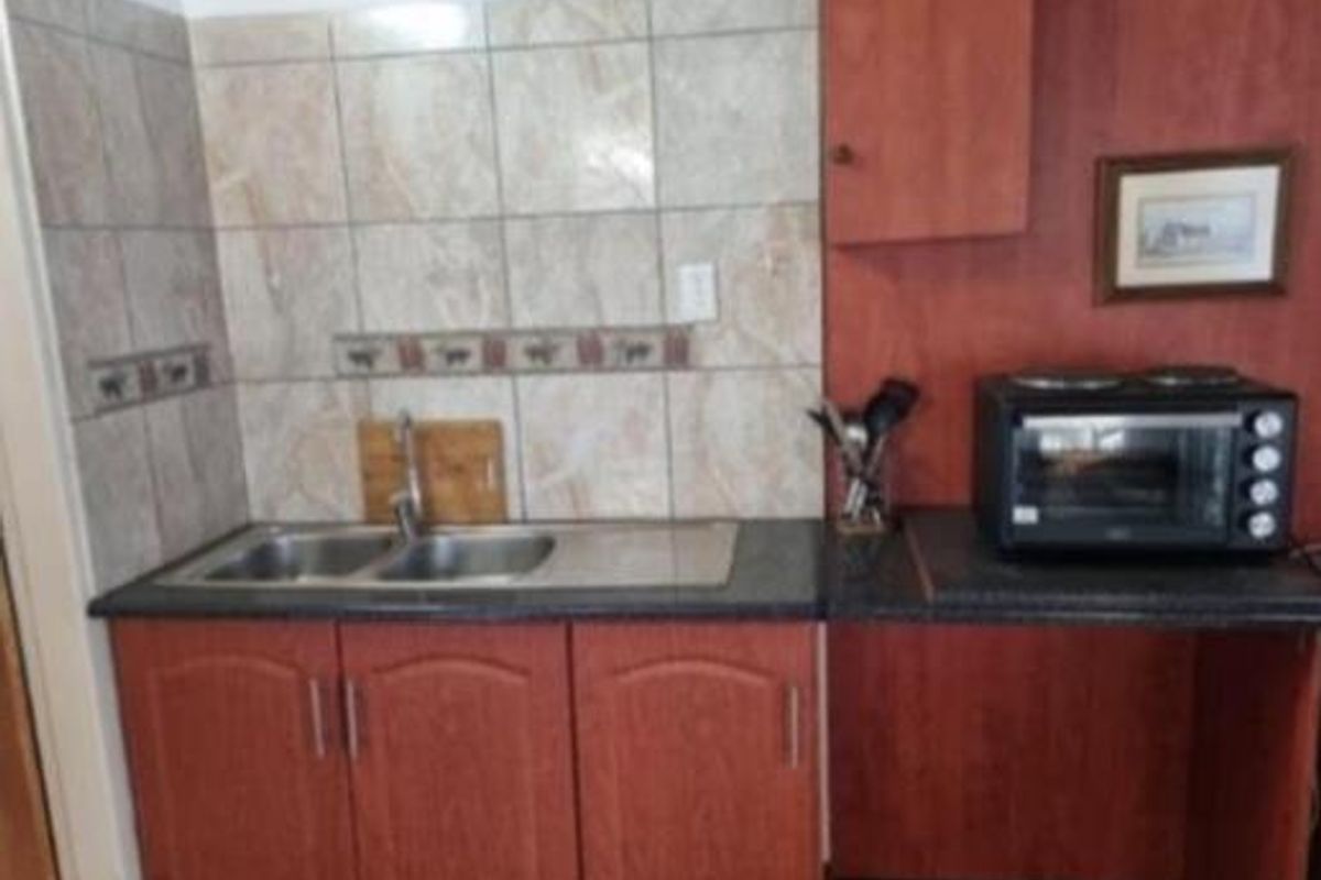 Compact kitchen area featuring laminate cabinetry, a double bowl stainless steel sink, and tiled backsplash with a functional countertop workspace.