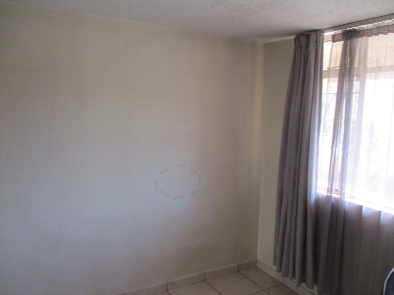 A simple, empty bedroom featuring tiled flooring and a window with installed curtain tracks, providing a blank canvas for personalization.