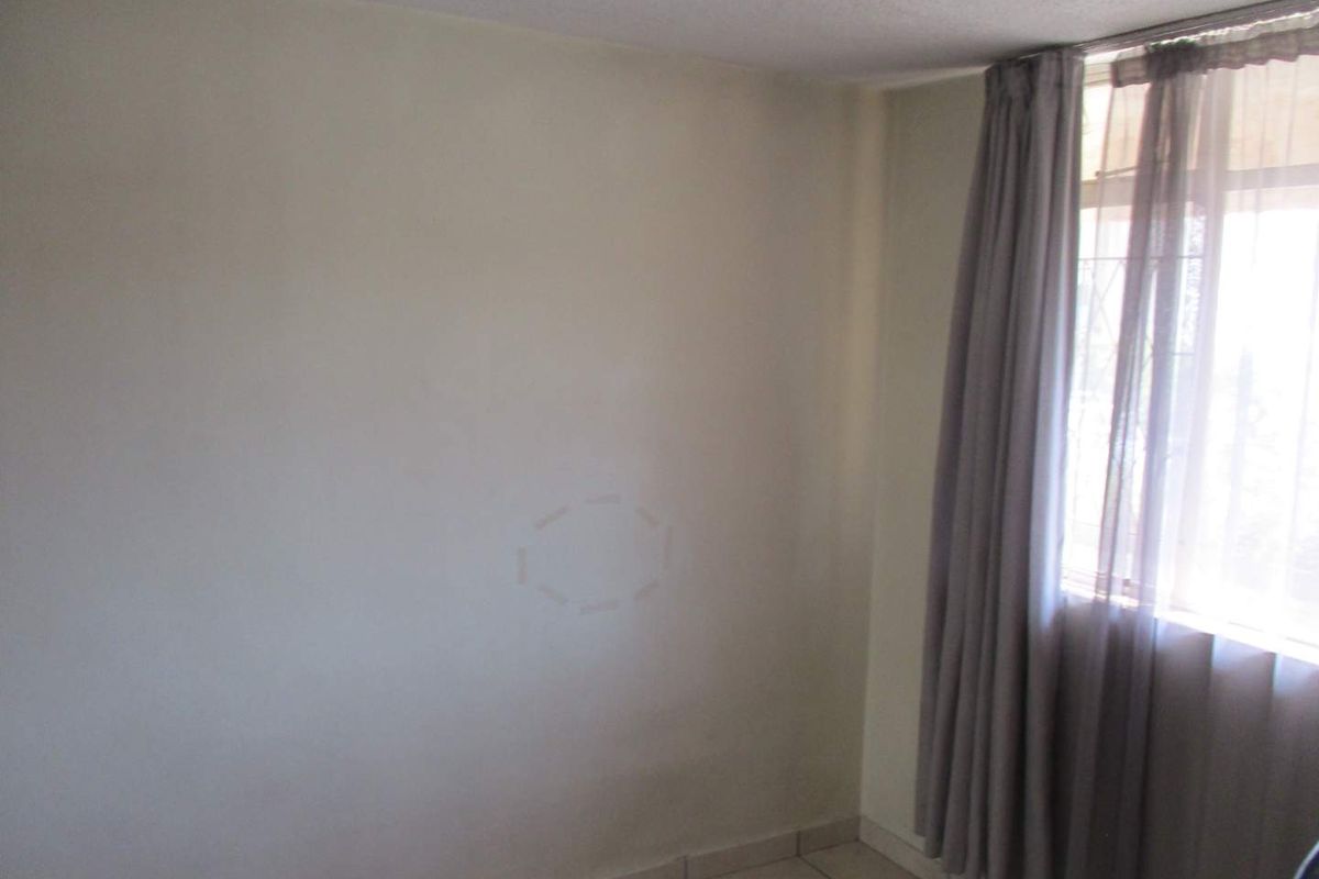 A simple, empty bedroom featuring tiled flooring and a window with installed curtain tracks, providing a blank canvas for personalization.