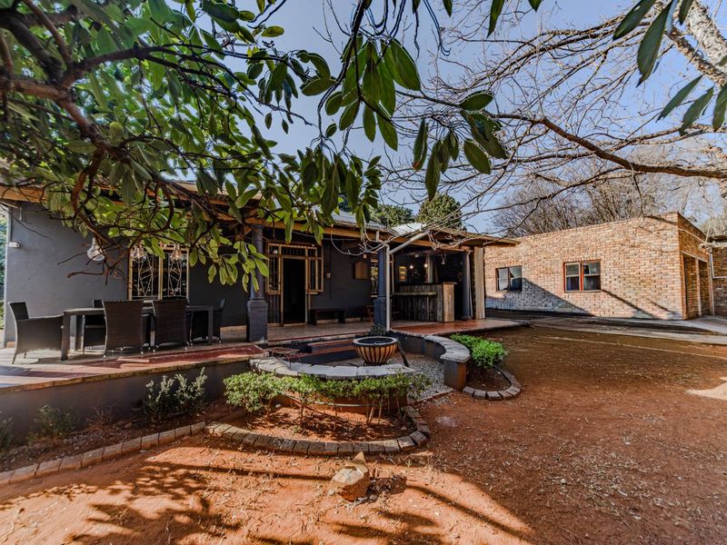A spacious covered patio area featuring a built-in bar, overlooking a garden with a fire pit and brick-finished exterior walls.