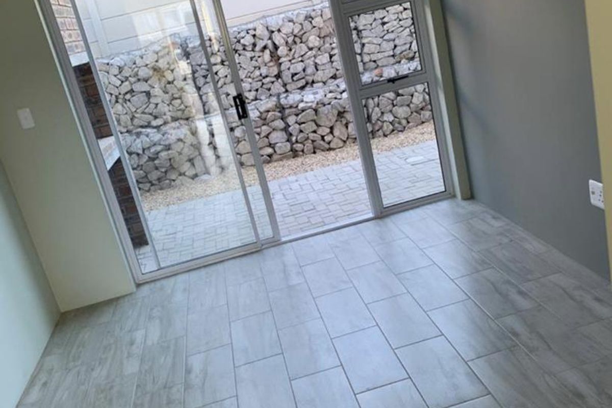 An empty living room featuring modern wood-look ceramic floor tiles and a large sliding glass door providing access to an outdoor patio area.